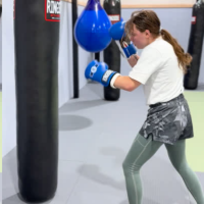 Child practicing punches on focus pads during youth MMA class.